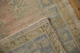 Distressed Oushak rug corner, showing worn pile in blush, blue, ochre tones, and intact selvage.