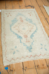 Angled view of a distressed Oushak rug with an ivory field and geometric sky blue and copper medallion.