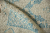 Even wear on the hand-knotted ivory and sky blue pile of a distressed Oushak rug.
