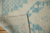 Folded corner of a distressed Oushak rug reveals its hand-knotted construction and woven back.