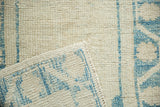 Corner of a distressed Oushak rug folded back, showing the hand-knotted foundation and the ivory and blue pile.
