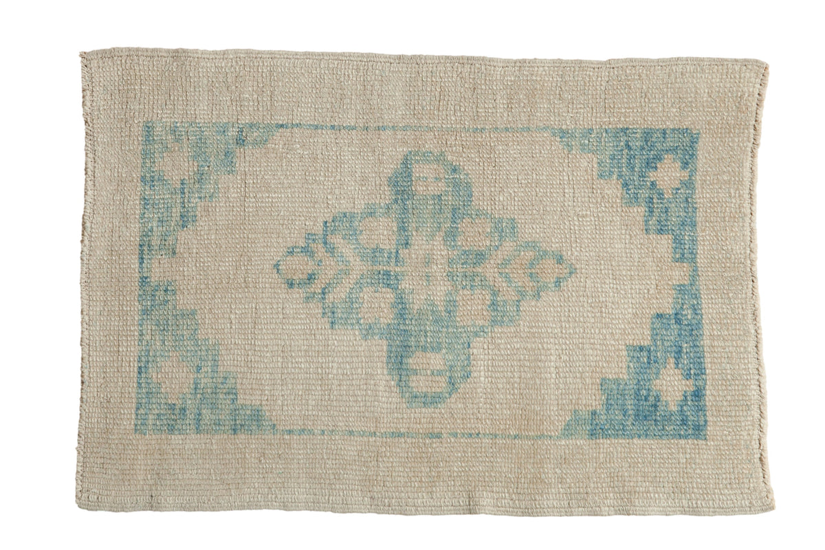 Distressed Oushak rug with a blue starburst medallion and spandrels on an antique ivory, low-pile field.