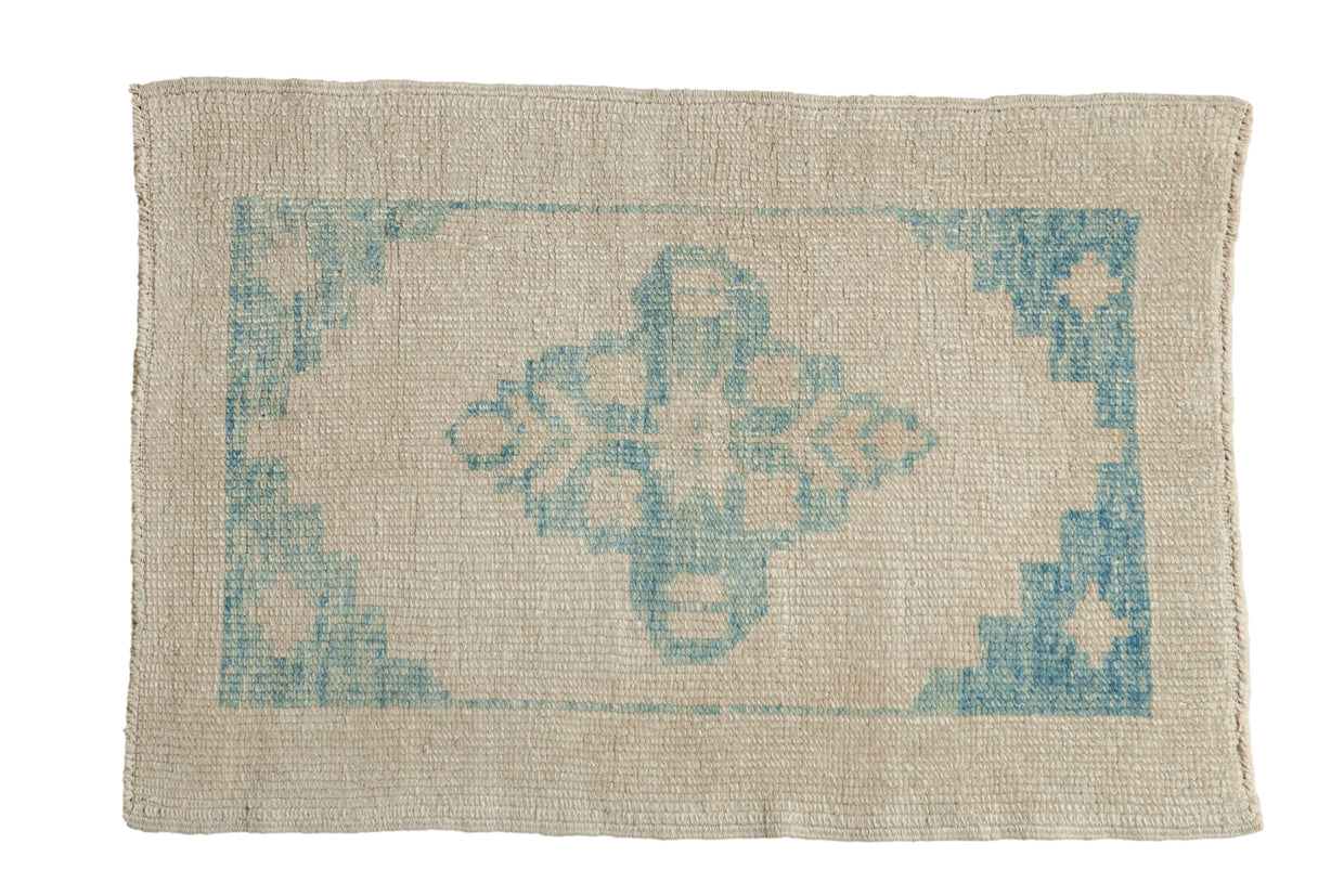 Distressed Oushak rug with a blue starburst medallion and spandrels on an antique ivory, low-pile field.