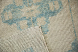 A folded corner of the distressed Oushak rug reveals its hand-knotted back and low pile.
