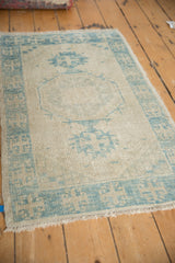 Distressed Oushak rug with pale blue blossoms on antique ivory, faint foundation visible.