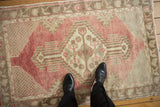 A person's view of a vintage distressed Oushak rug, highlighting its faded red and beige tones.