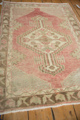 Angled view of a distressed Oushak rug's geometric medallion in faded red, beige, and silver tones.