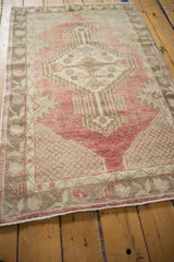 Angled view of a distressed vintage Oushak rug with a faded cherry red field and beige geometric patterns.