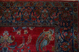 Close view of an antique Kashan rug's corner, with a sapphire blue border and paisley boteh on a red field.