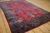 Antique Persian Kashan rug from an angle, showing the pomegranate red field and sapphire border.