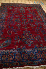 Angled view of a sapphire blue paisley boteh and florals on a rich red antique Kashan rug.