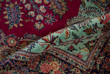 Curled corner of a Dabir Kashan rug showing the intricate mint green border and cherry red field.