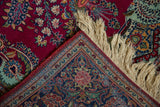 Folded corner of a vintage Dabir Kashan rug showing its cherry red field, detailed navy border, and ivory fringe.