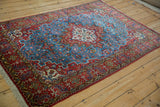 Angled view of a vintage Qom rug's geometric medallion, blue field, and cherry red border.