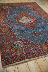 Angled view of a vintage Persian Qom rug highlighting the medallion, blue field, and red borders.