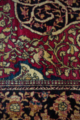 Intricate floral arabesques and scrolling vines in cochineal red and navy on an antique Isfahan rug.