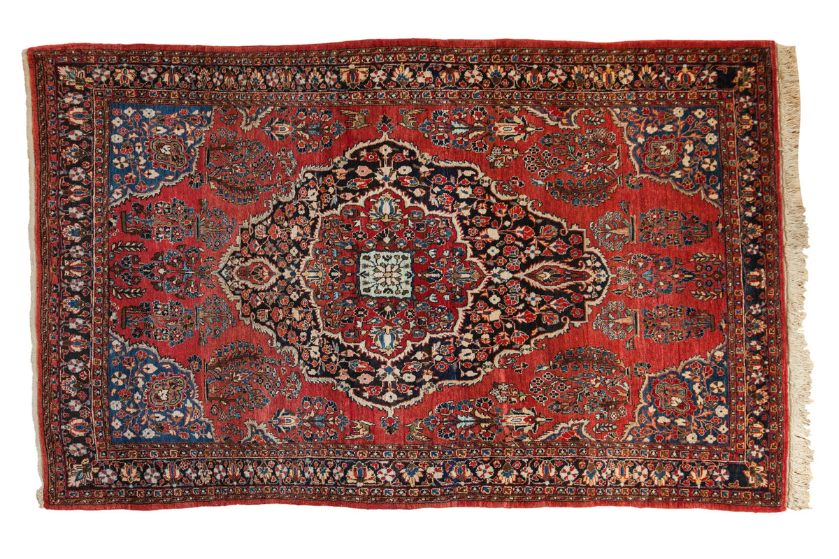 Vintage Sarouk rug with a navy medallion, floral motifs, and vivid blue corner spandrels on a brick red field.