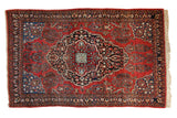 Vintage Sarouk rug with a navy medallion, floral motifs, and vivid blue corner spandrels on a brick red field.
