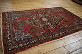 Angled view of a vintage Sarouk rug with a brick red field, navy medallion, and sapphire blue spandrels.