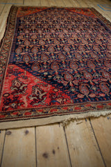 Antique Malayer rug's unsecured end with tattered fringe, red field, and navy boteh pattern.