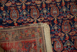 Folded corner of Malayer rug, showing navy pile, red boteh, and exposed flat-woven foundation.