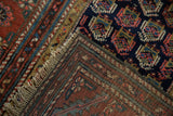 Antique Kurdish Hamadan rug's folded corner, revealing hand-knotted foundation, fringe, and geometric motifs.