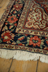 Angled detail of a vintage Sarouk rug corner showing the navy floral border and ivory fringe.
