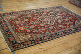 Vintage Sarouk rug from an angle, showcasing the cherry red floral field and dark navy border.