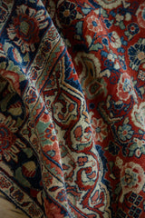 Folded vintage Sarouk rug showing intricate floral motifs in cherry red, navy blue, and ivory.