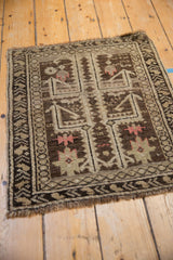 Time-softened tones and geometric forms of an antique Caucasian rug mat from an angled view.