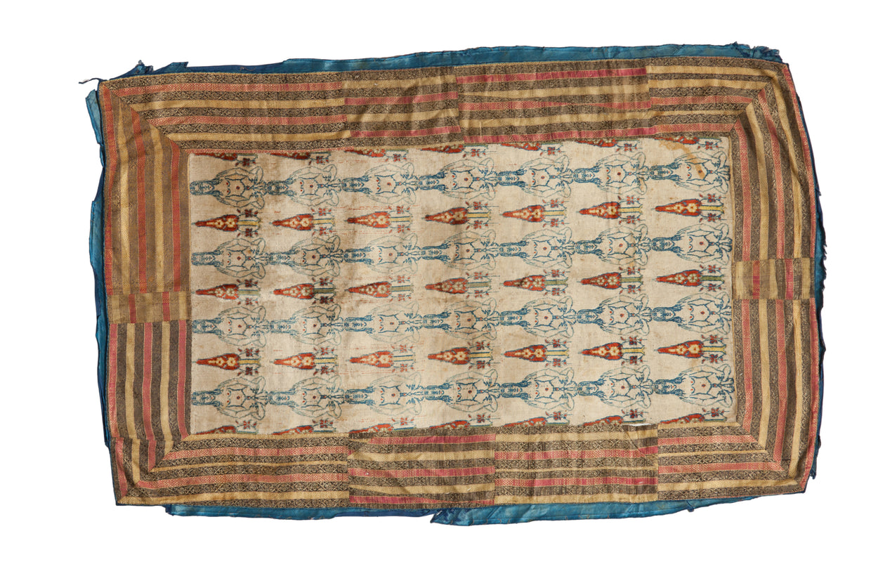An 18th century Persian velvet textile with stylized human figures and a warm, multi-striped border.
