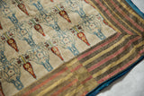 Corner of an antique Persian velvet textile with a warm striped border and visible blue backing.