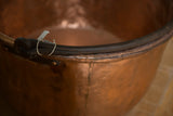 Detail of the antique kettle's dark blacksmithed handle and hammered copper rim.