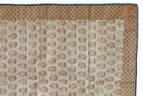 Corner of an antique Persian brocade showing its floral field, patterned border, and blue backing.