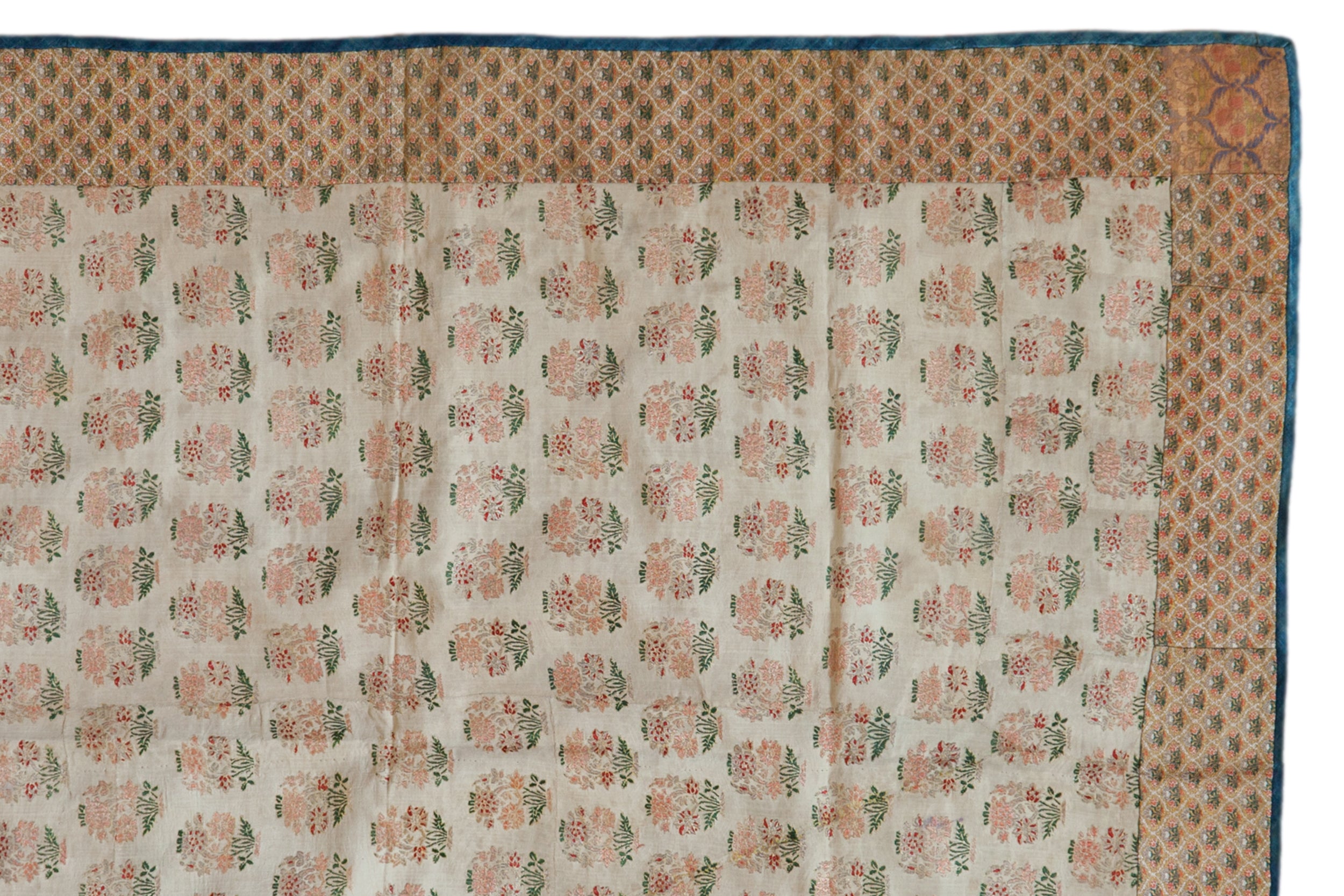 Corner of an antique Persian brocade showing its floral field, patterned border, and blue backing.
