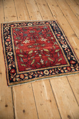Angled view of a square antique Farahan Sarouk rug with a red floral field and navy border.