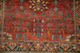 Detailed floral vines in dusty jade green and saffron on the rug's brick-red field.