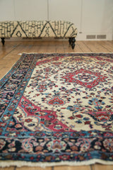 Low angle view of an antique Sarouk rug showing its red medallion, floral patterns, and ivory field.