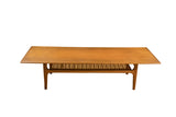 Vintage Mid-Century Modern sled coffee table with a warm teak top and lower woven cane shelf.