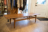 Side view of the vintage Danish teak coffee table showing its sled legs and woven shelf.