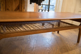 A low perspective on the woven cane shelf of the mid-century teak table.