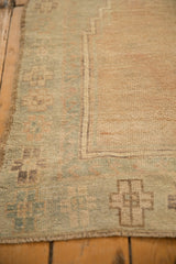 Corner detail of a distressed Oushak rug showing its low pile and seafoam green geometric border design.