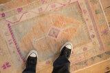A vintage distressed Oushak rug's worn texture and soft palette of cantaloupe, silver, and fuchsia.