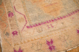 Low pile texture of a distressed Oushak rug showing magenta details on a dusty gold field.
