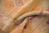 Folded vintage Oushak rug showing distressed, low-pile texture in dusty gold with magenta accents.