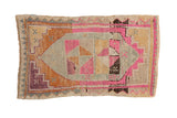 Vintage distressed Kars rug with an asymmetric pinwheel medallion in pink, orange, silver, and aubergine purple.
