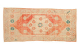 Distressed Oushak rug runner with a red shield medallion and teal floral details on a worn ivory ground.