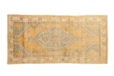 Distressed vintage Oushak rug with a shield medallion in faded saffron yellow and turquoise green.