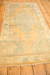 A lengthwise perspective of a distressed Oushak rug showing its faded saffron and turquoise palette.