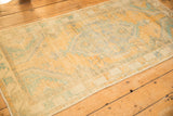 Angled view showing the low pile and faded saffron and turquoise design of a distressed Oushak rug.